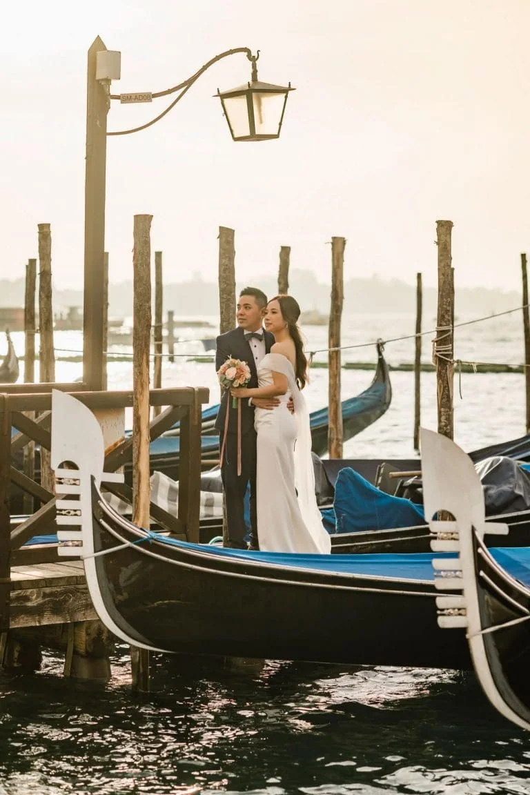 Couple by the water with Venetian gondolas in the background – Venice Wedding Photography Engagement.