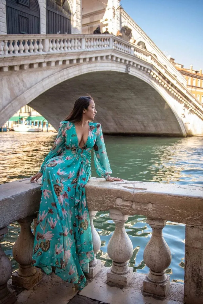 Young woman sitting elegantly in front of the Rialto Bridge during a romantic Venice engagement session.