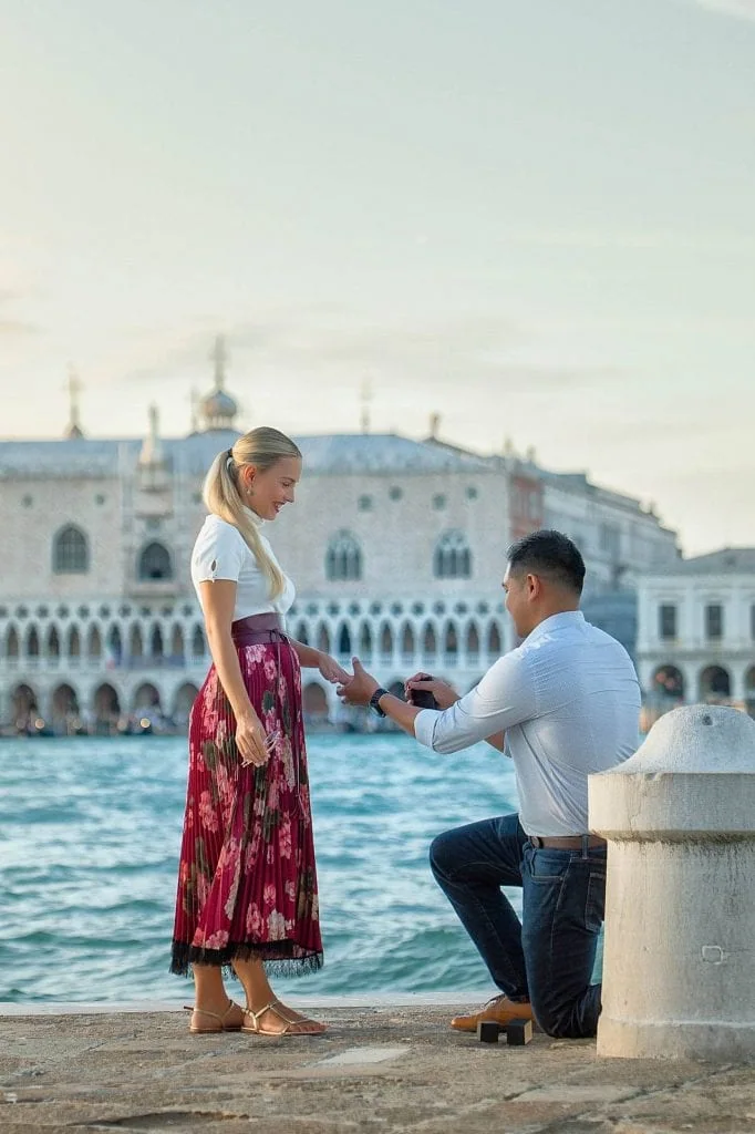 A couple holding hands by the Grand Canal with Saint Mark's Basilica and a vivid red sky in the background during a photo session in Venice.
