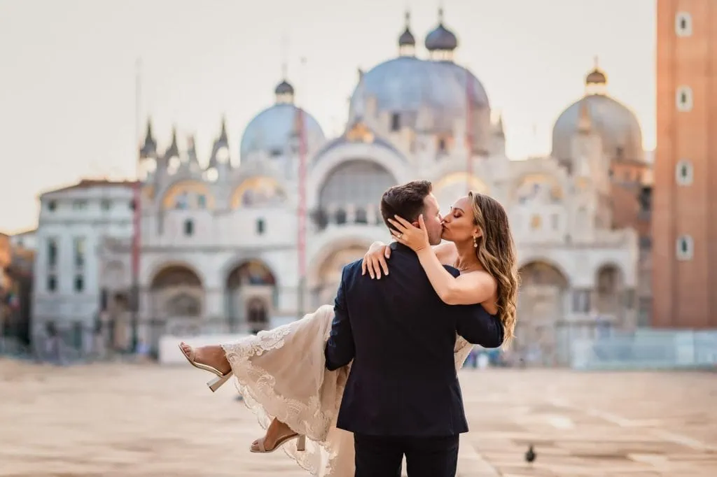 Bride and groom walk hand in hand through an empty Piazza San Marco, with the Bridge of Sighs in the background.