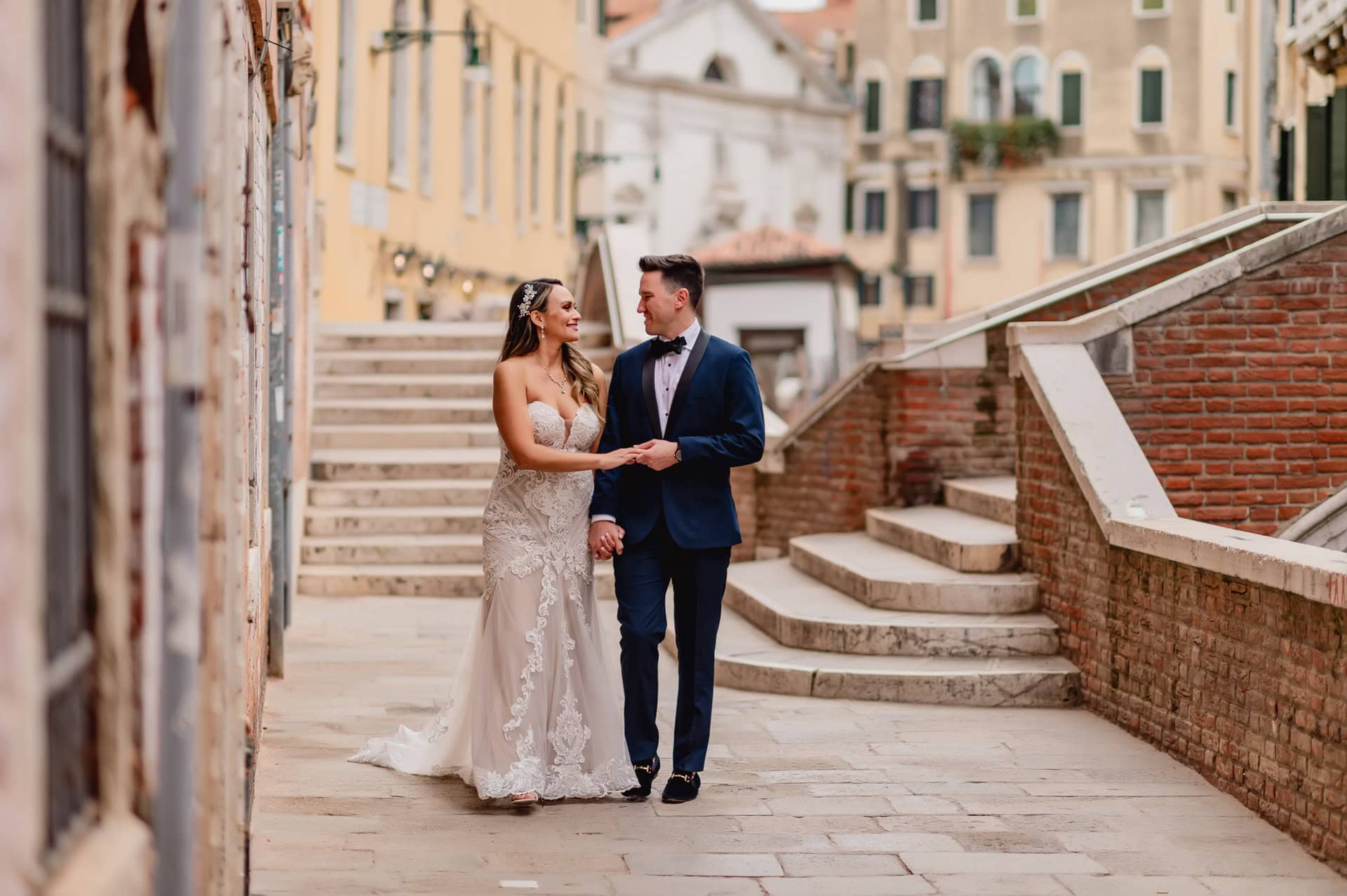 Bride and groom walking hand in hand through a romantic Venetian alley with canals in the background.