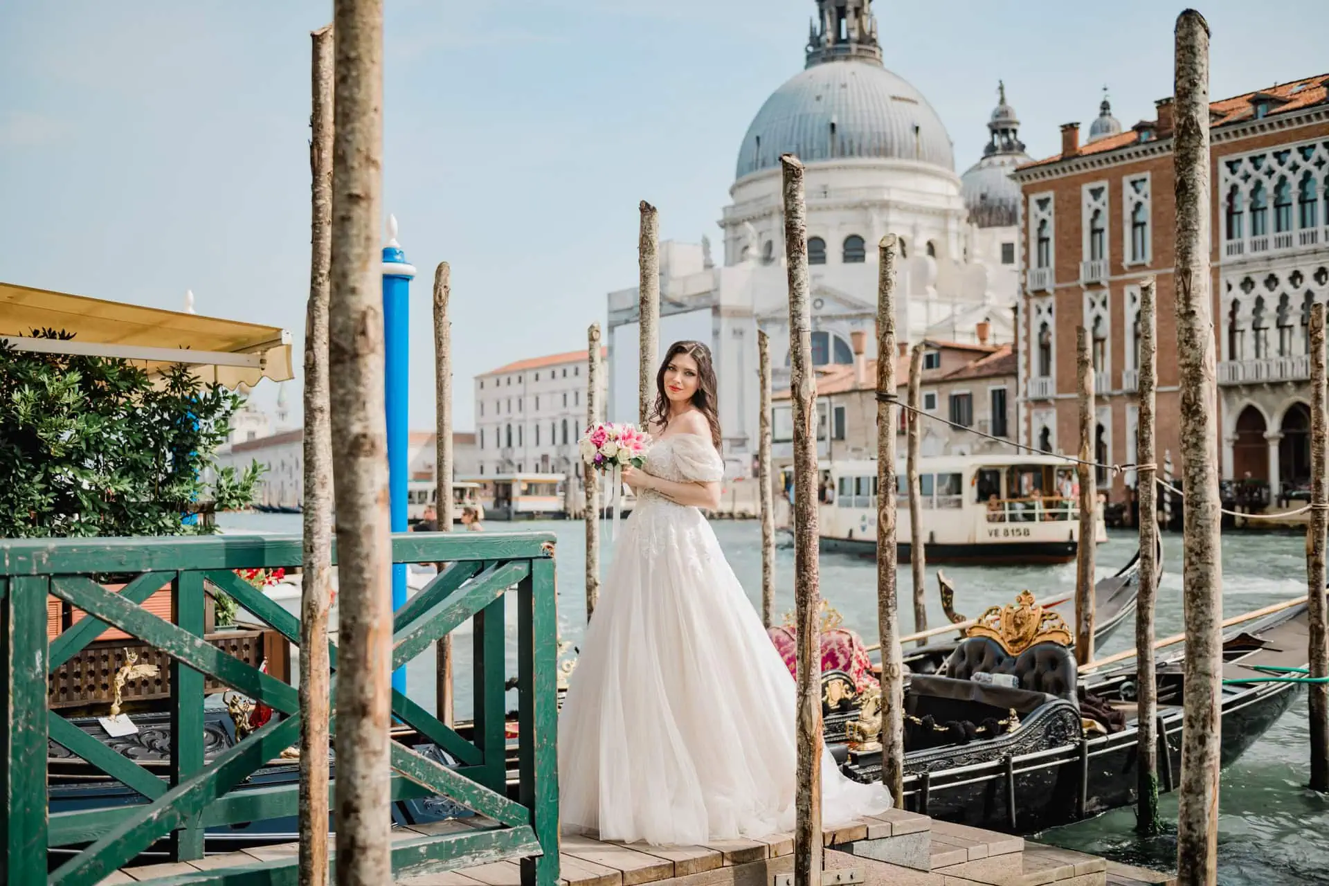 Venice wedding photoshoot with bride holding a bouquet near canal, gondolas, and historic architecture.