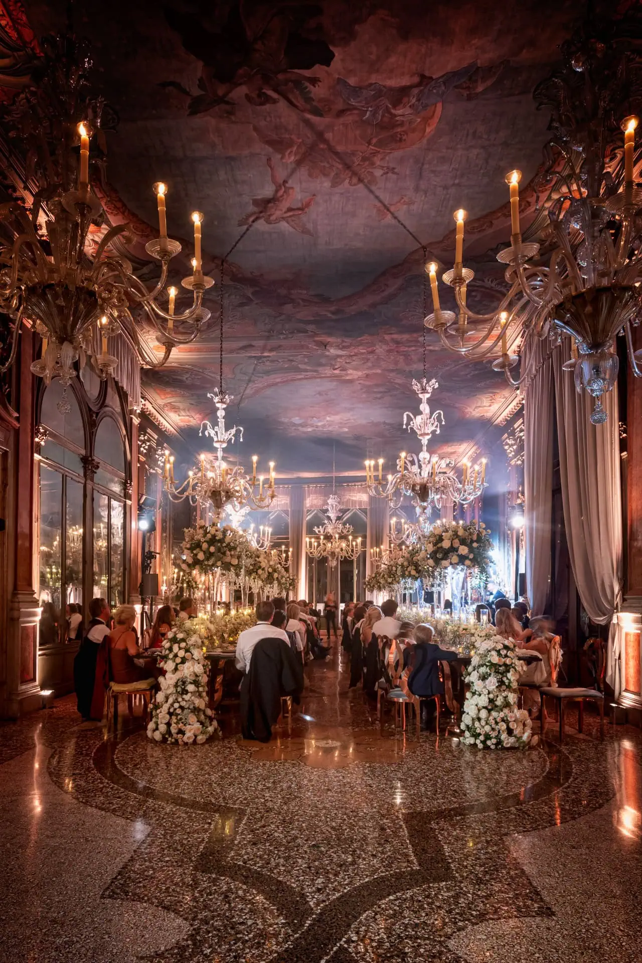 Elegant Venetian wedding reception with grand chandeliers and floral decor.