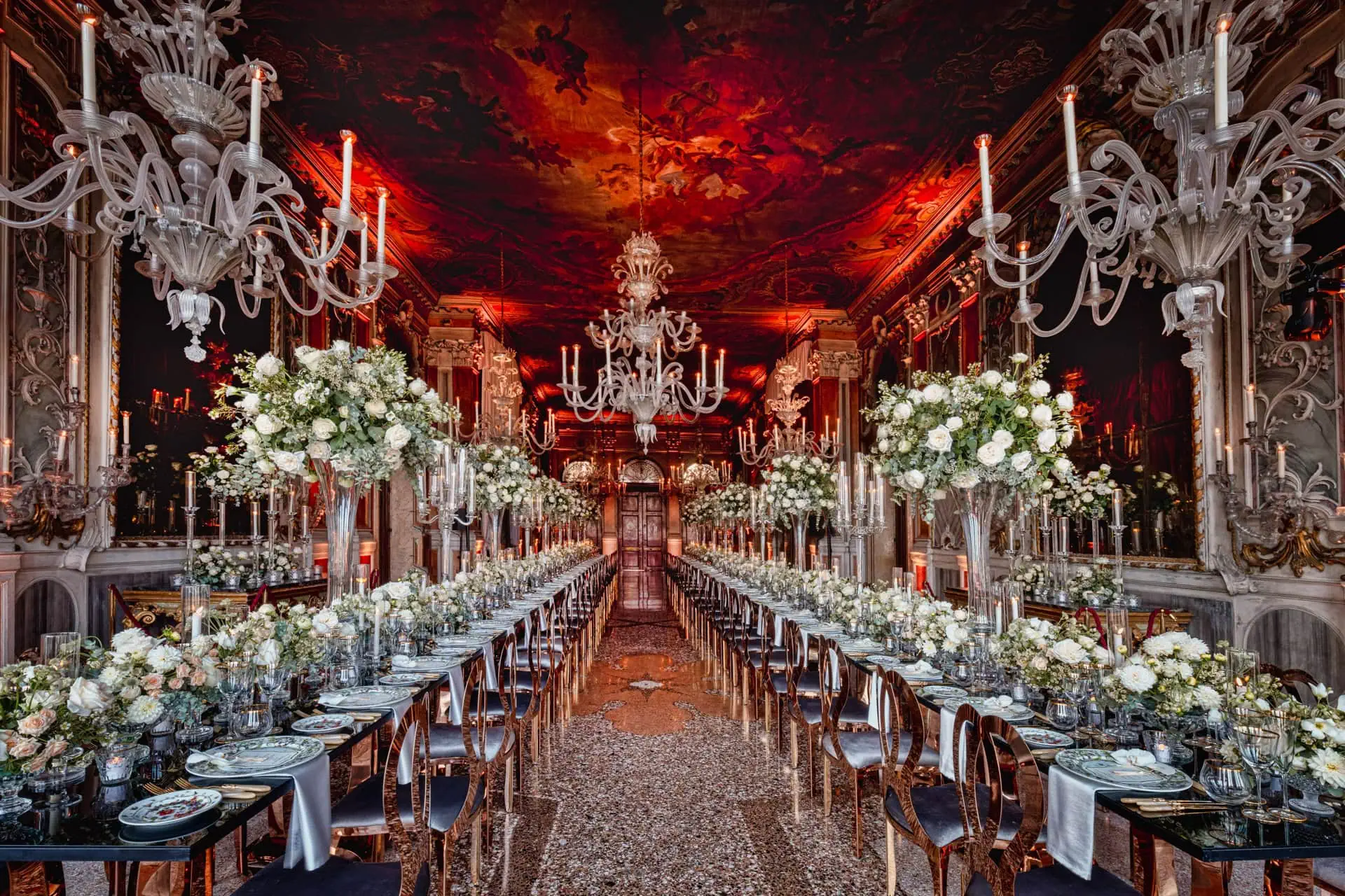 Luxurious ornate wedding reception hall with chandeliers and floral centerpieces.