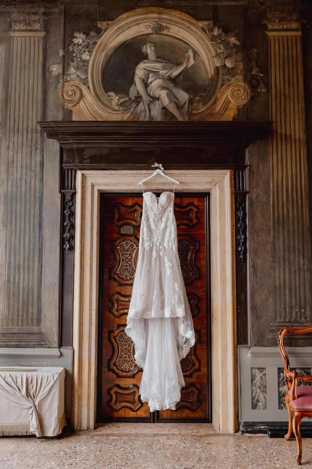 Elegant lace wedding dress hanging on a door in a historic Venetian interior.