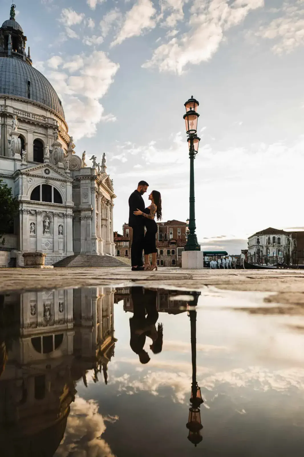 Venice couple portrait during sunset with historic architecture and reflection in puddle.