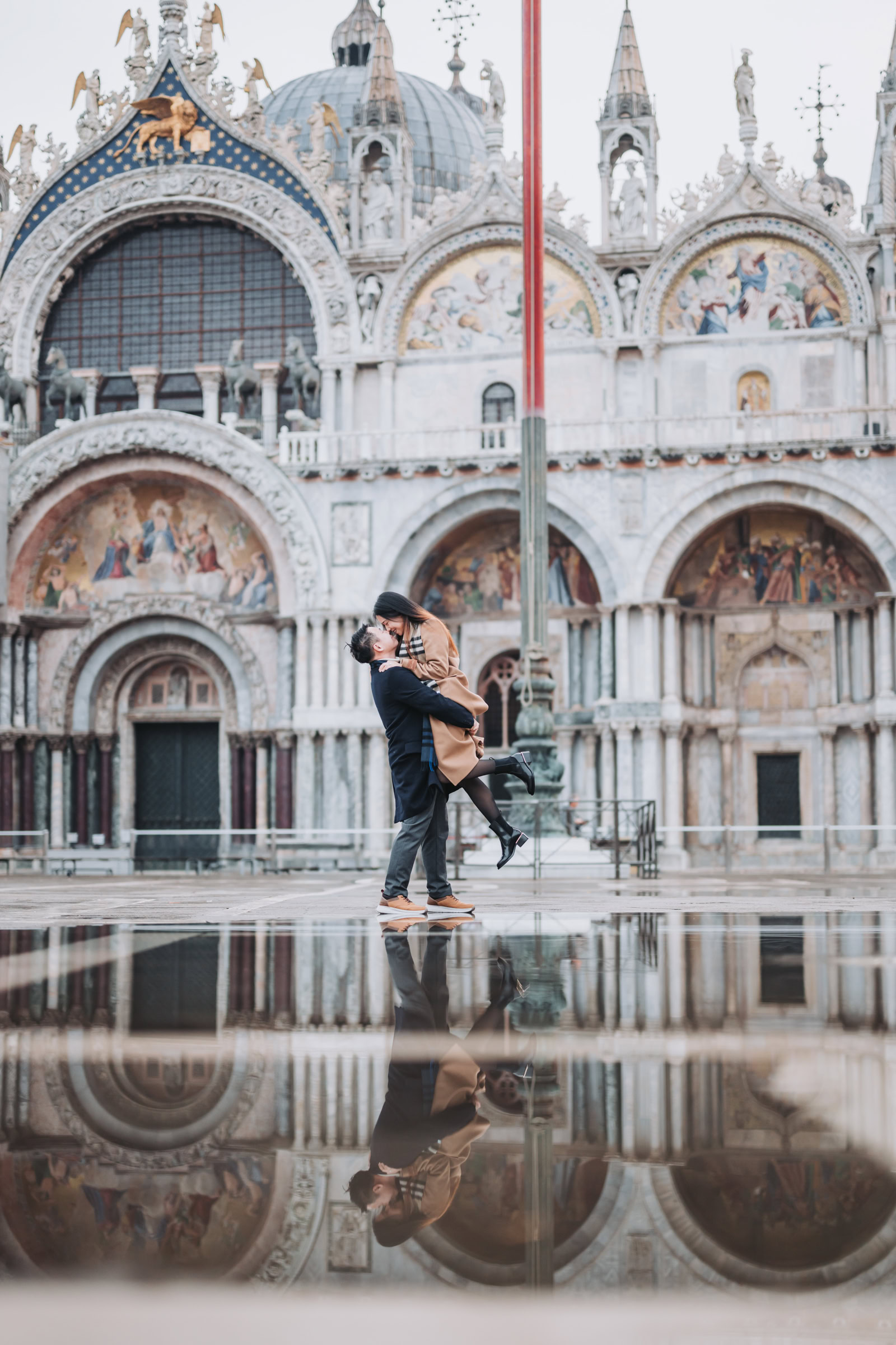 Man lifting woman near gondola moorings at San Marco with the Basilica di San Marco visible in the background, early morning light