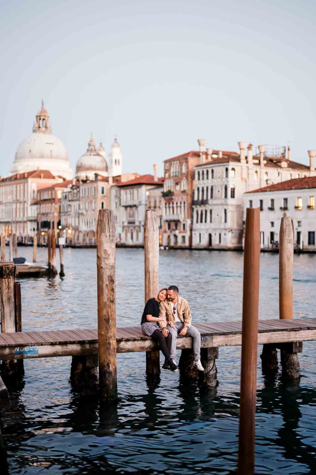 Venice couple enjoying a romantic moment on a dock with historic cityscape in the background.