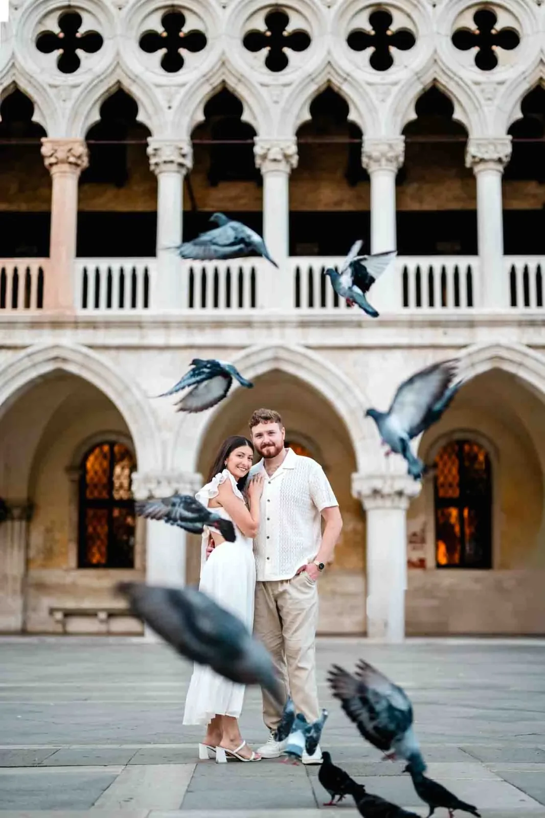 Proud couple embracing in front of historic Venetian architecture with flying pigeons in Venice, Italy.
