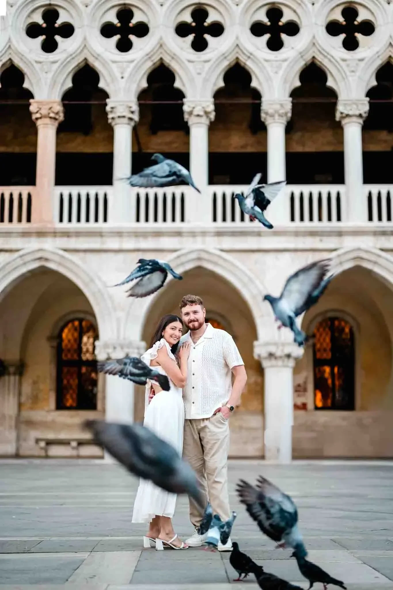 Proud couple embracing in front of historic Venetian architecture with flying pigeons in Venice, Italy.