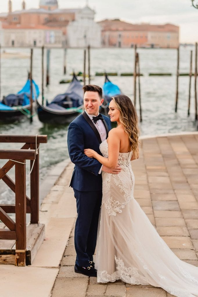 Bride and groom walk hand in hand through an empty Piazza San Marco, with the Bridge of Sighs in the background.