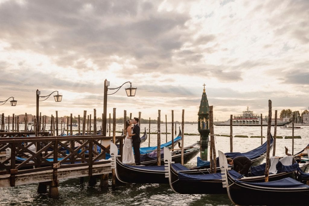 Bride and groom walk hand in hand through an empty Piazza San Marco, with the Bridge of Sighs in the background.