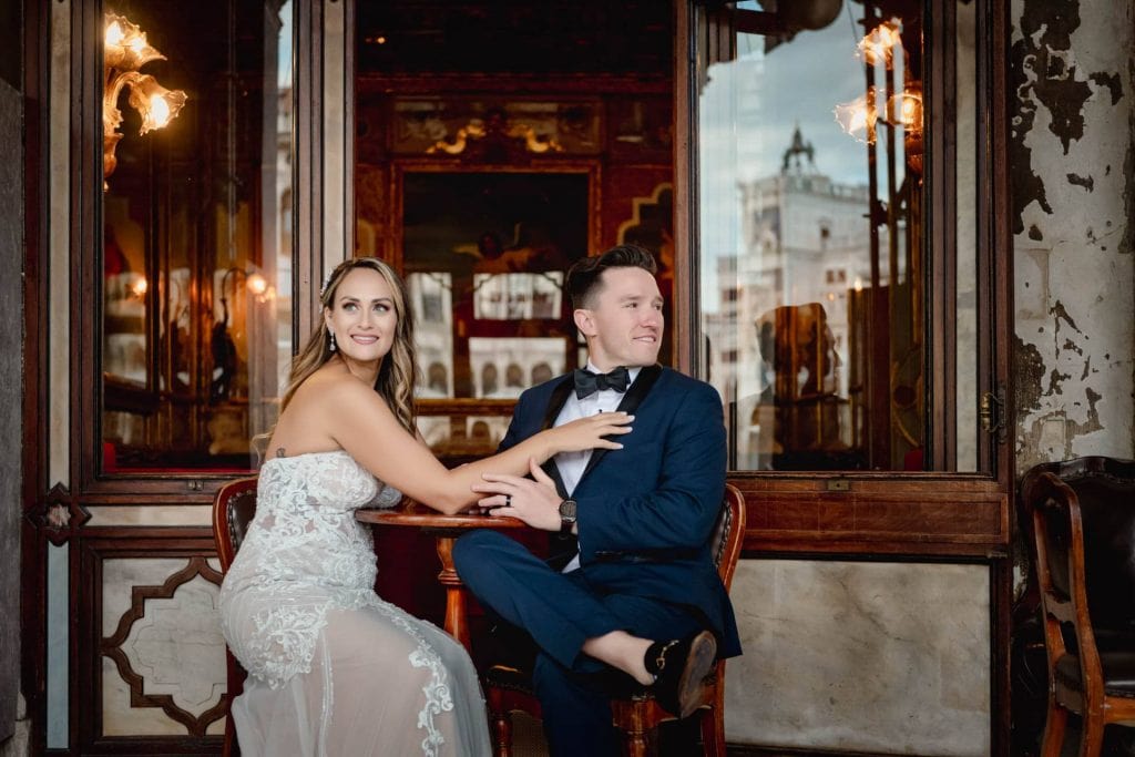 Bride and groom walk hand in hand through an empty Piazza San Marco, with the Bridge of Sighs in the background.