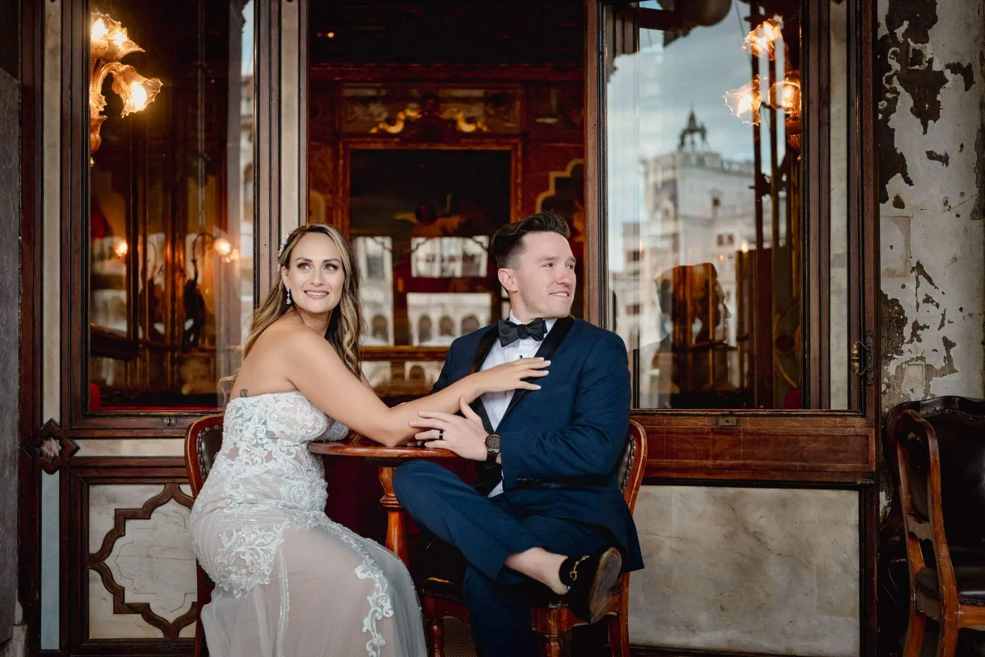 Bride and groom walk hand in hand through an empty Piazza San Marco, with the Bridge of Sighs in the background.