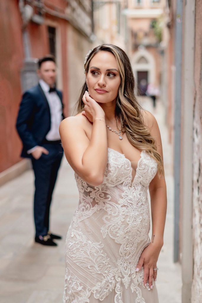 Bride and groom walk hand in hand through an empty Piazza San Marco, with the Bridge of Sighs in the background.