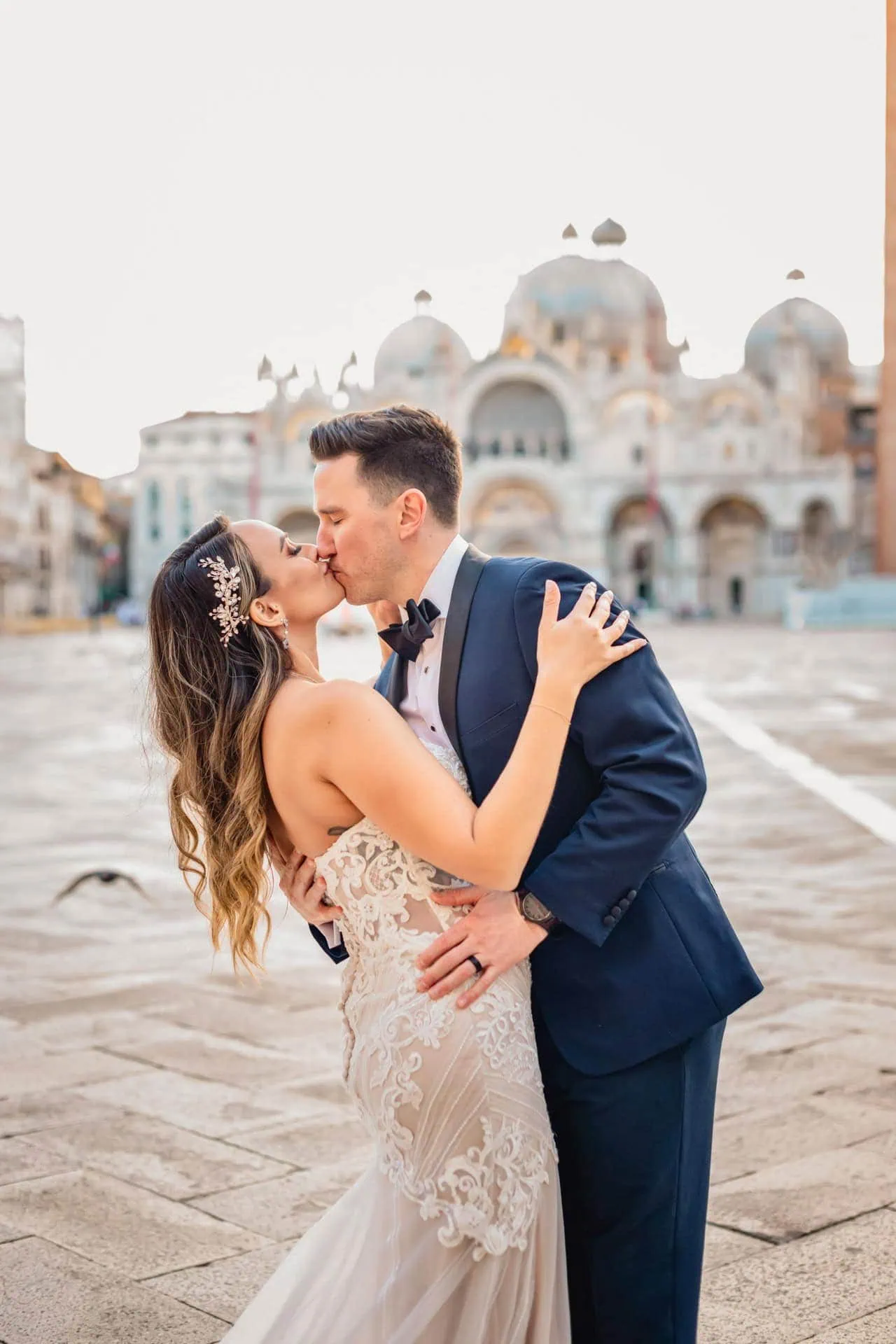 Bride and groom walk hand in hand through an empty Piazza San Marco, with the Bridge of Sighs in the background.