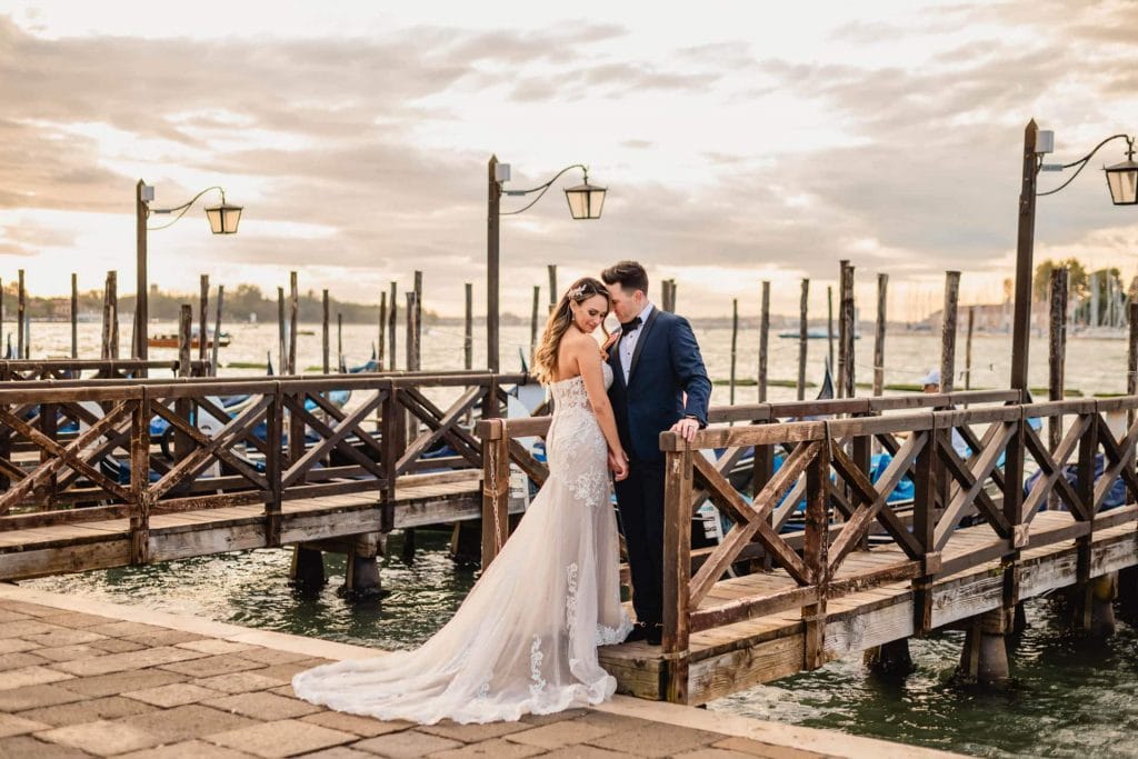Bride and groom walk hand in hand through an empty Piazza San Marco, with the Bridge of Sighs in the background.