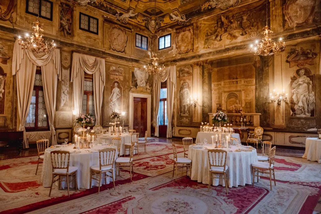 Elegant wedding table setting in a luxurious Venetian palace with floral arrangements and fine tableware.