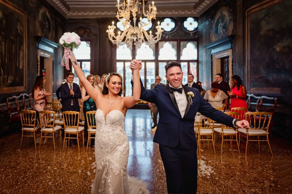 Bride and groom exchange vows in an ornate Venetian palace adorned with frescoes and sculptures.