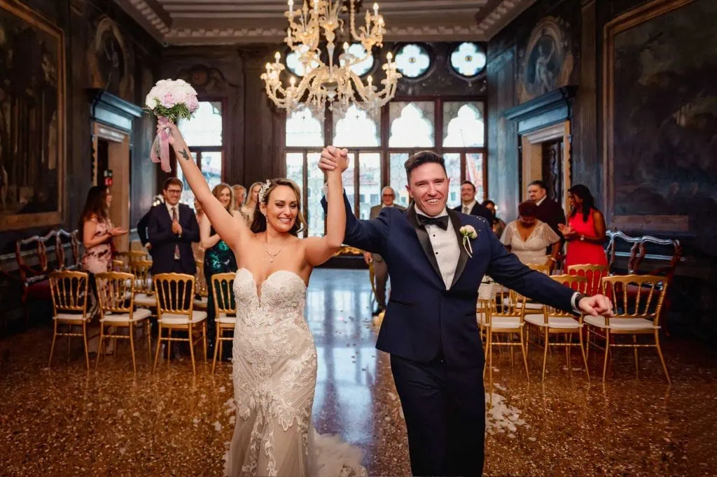 Bride and groom exchange vows in an ornate Venetian palace adorned with frescoes and sculptures.