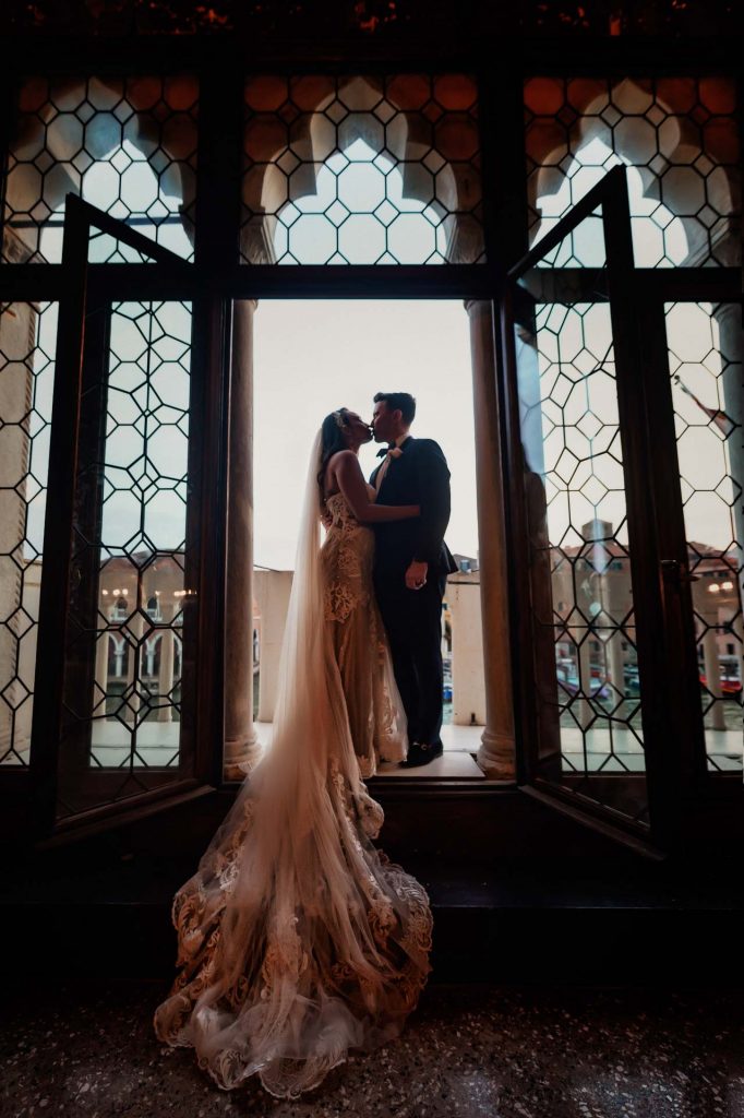 Bride and groom embrace on a balcony with a view of Venice’s Grand Canal at sunset.