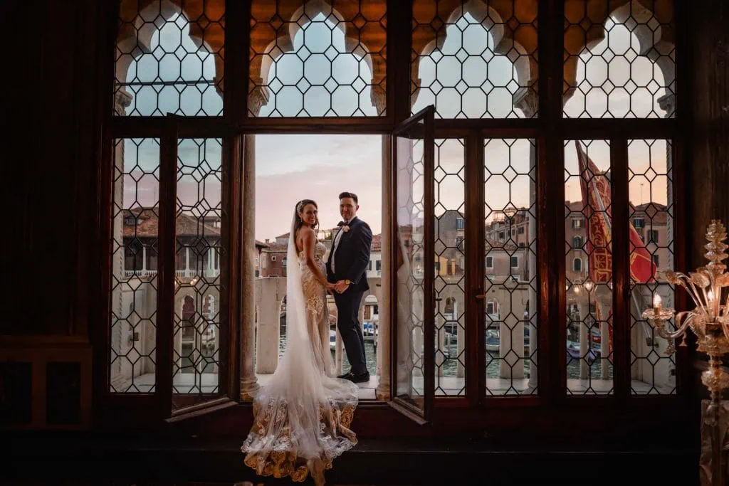 Bride and groom embrace on a balcony with a view of Venice’s Grand Canal at sunset.
