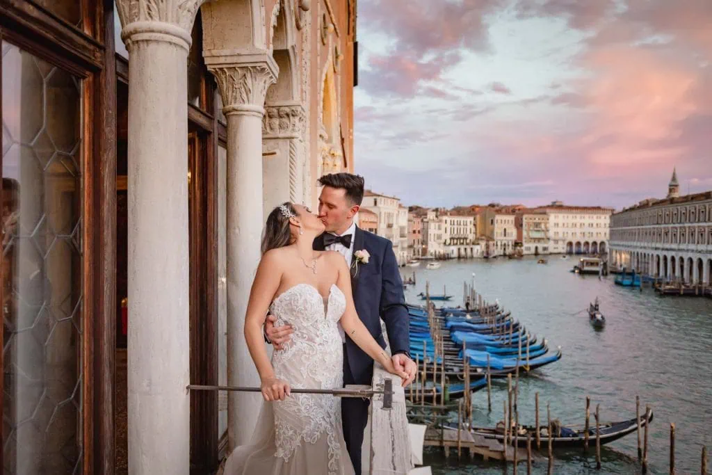 Bride and groom embrace on a balcony with a view of Venice’s Grand Canal at sunset.