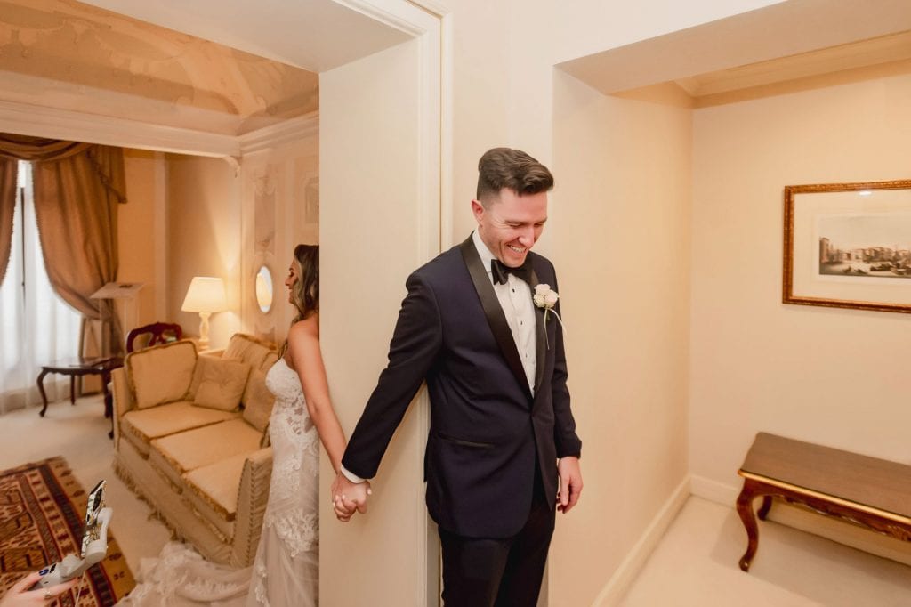 Bride and groom hold hands around a corner for their "first touch" moment in a luxurious Venetian hotel.