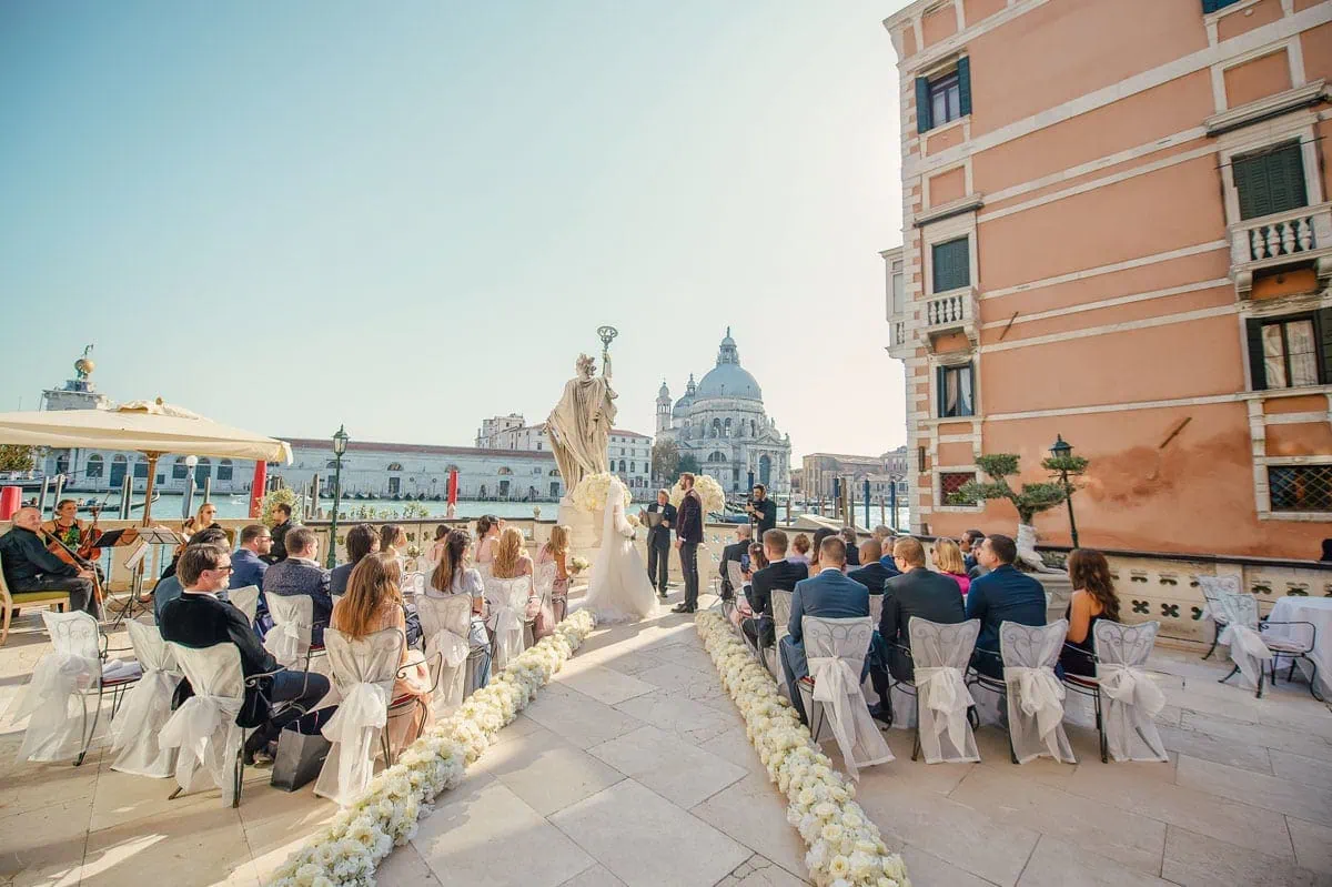 Elegant Venice wedding ceremony overlooking the canal with guests, floral decor, and historic architecture.