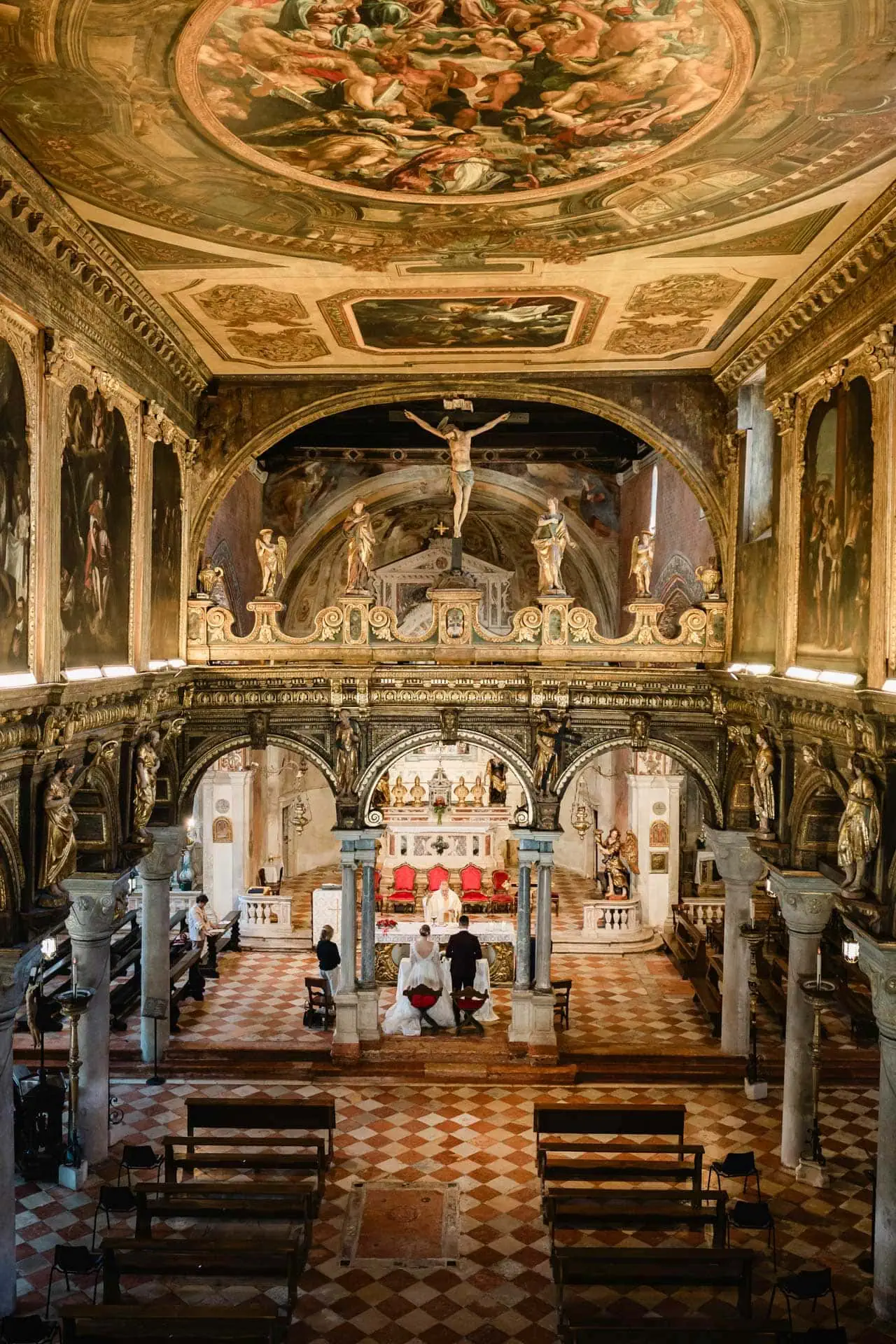 Venice wedding ceremony inside historic church with elaborate ceiling artwork and religious statues.