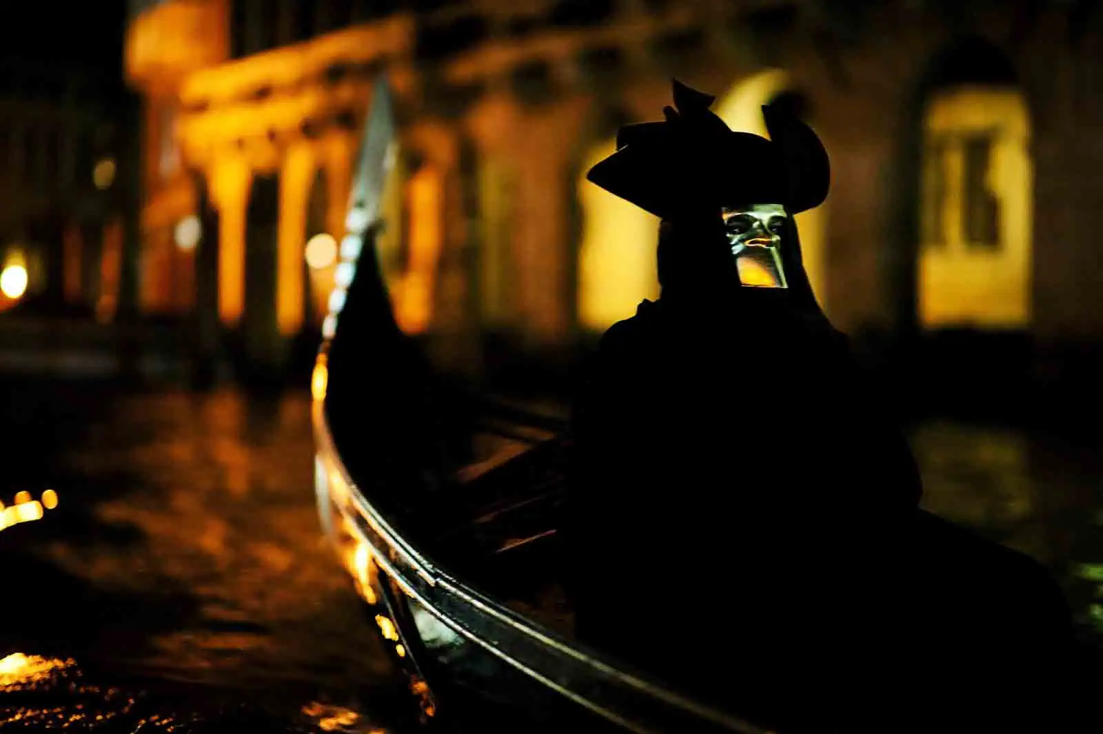 A masked Venice Carnival participant enjoying a gondola ride at sunset along the Grand Canal.