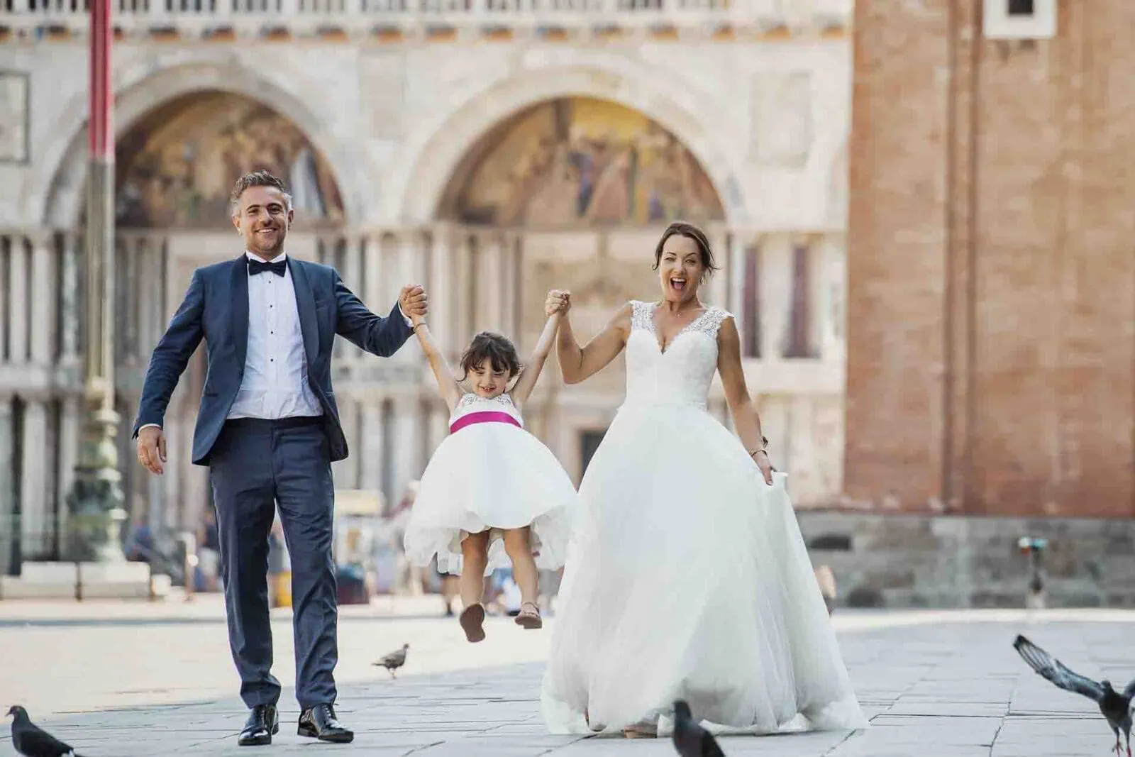 Parents holding hands with their daughter in St. Mark’s Square, Venice.