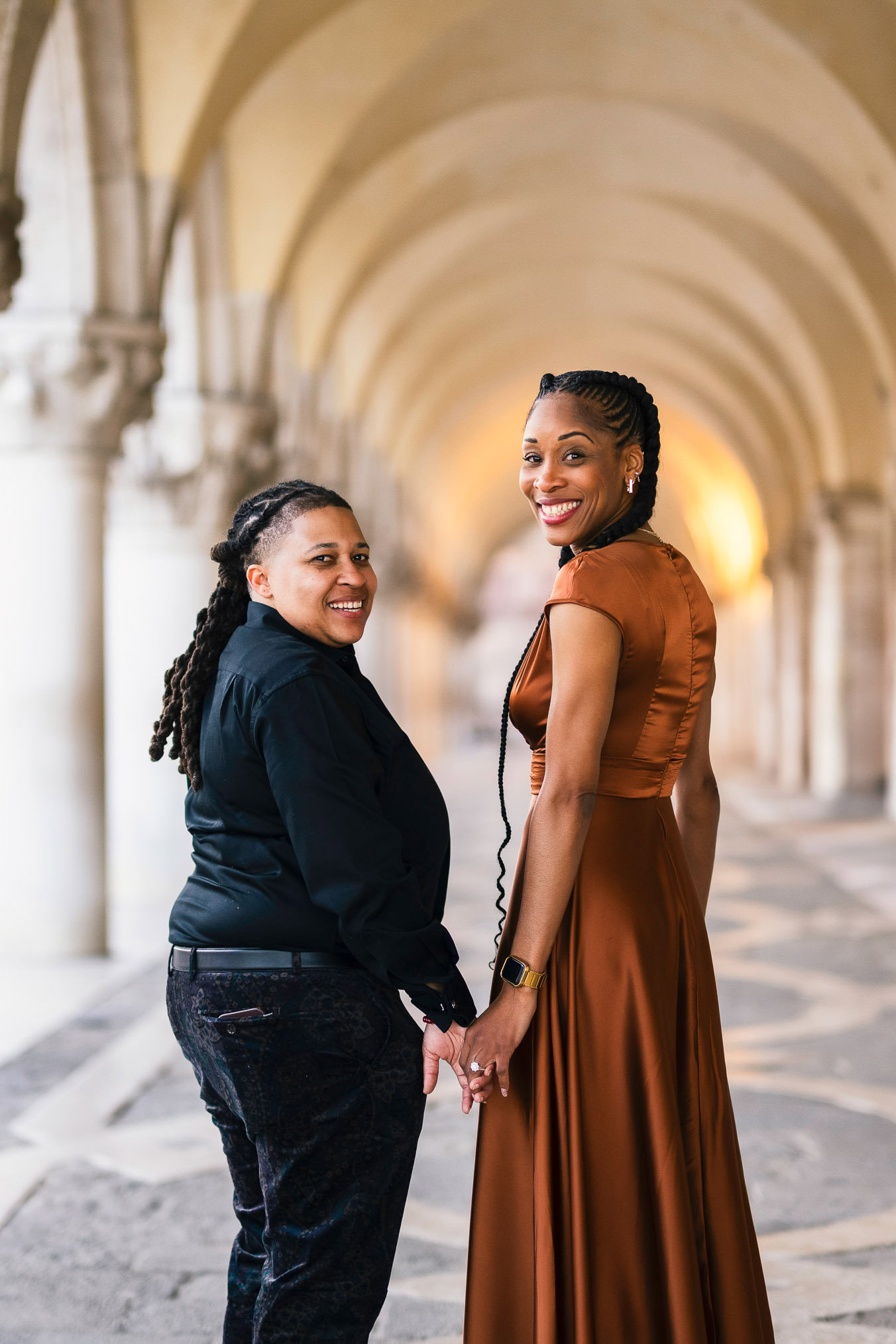 Two women in love under the arcades of San Marco with Bridge of Sighs behind them