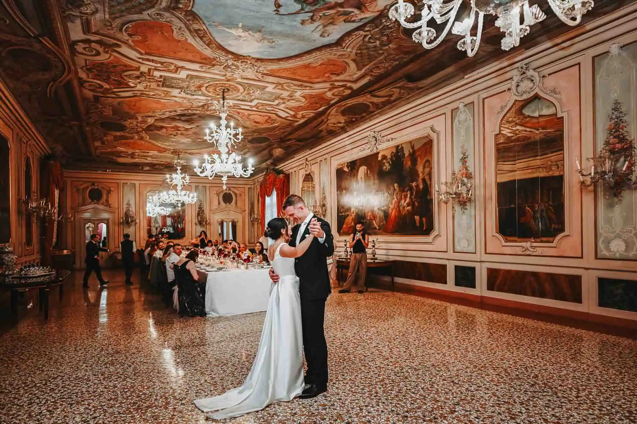 Elegant couple sharing a dance at Luna Baglioni Hotel, ornately decorated ballroom with chandeliers and classical artwork.