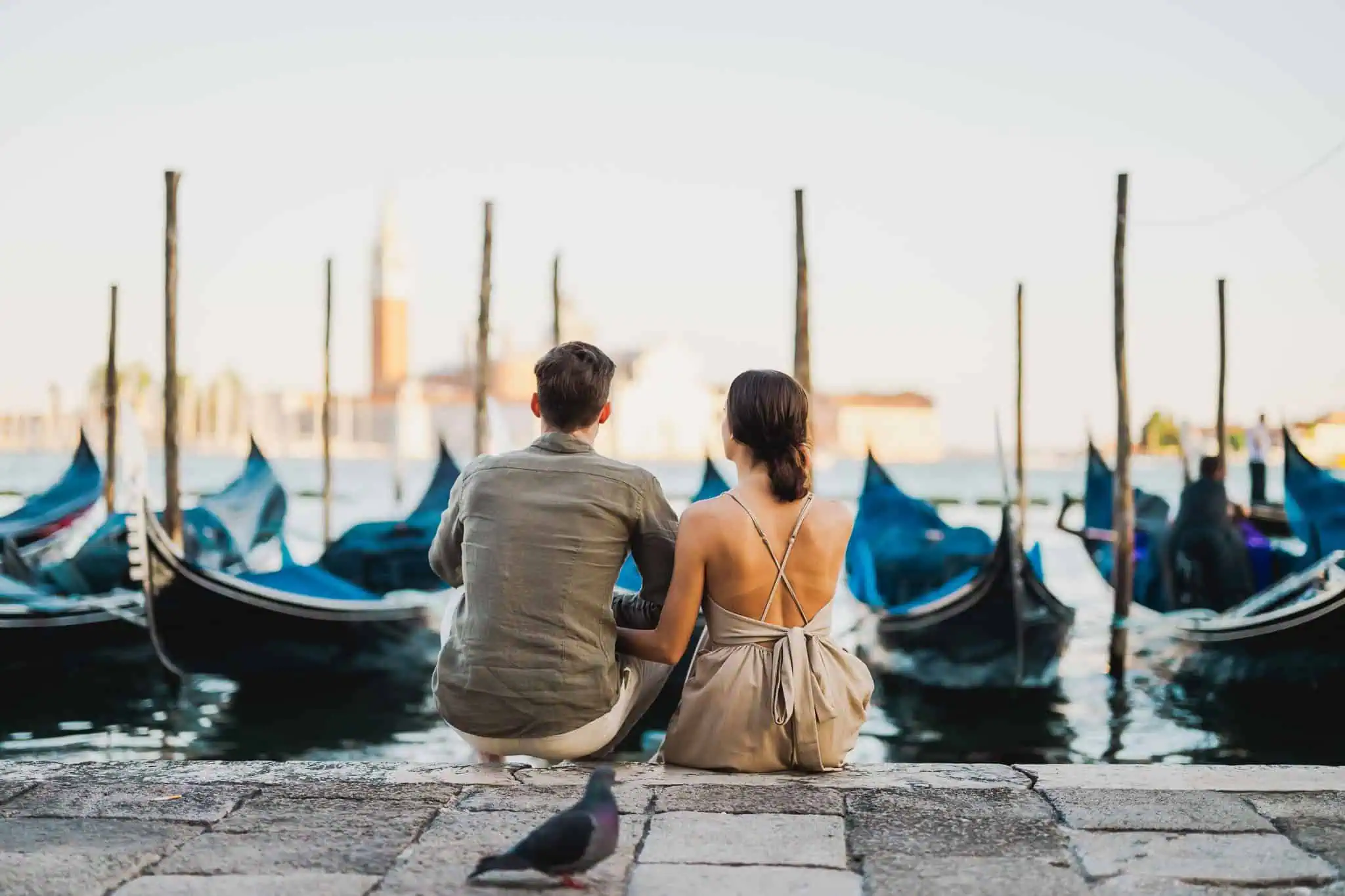 Romantic couple sitting by Venice canals, enjoying gondolas and cityscape, perfect wedding proposal backdrop.