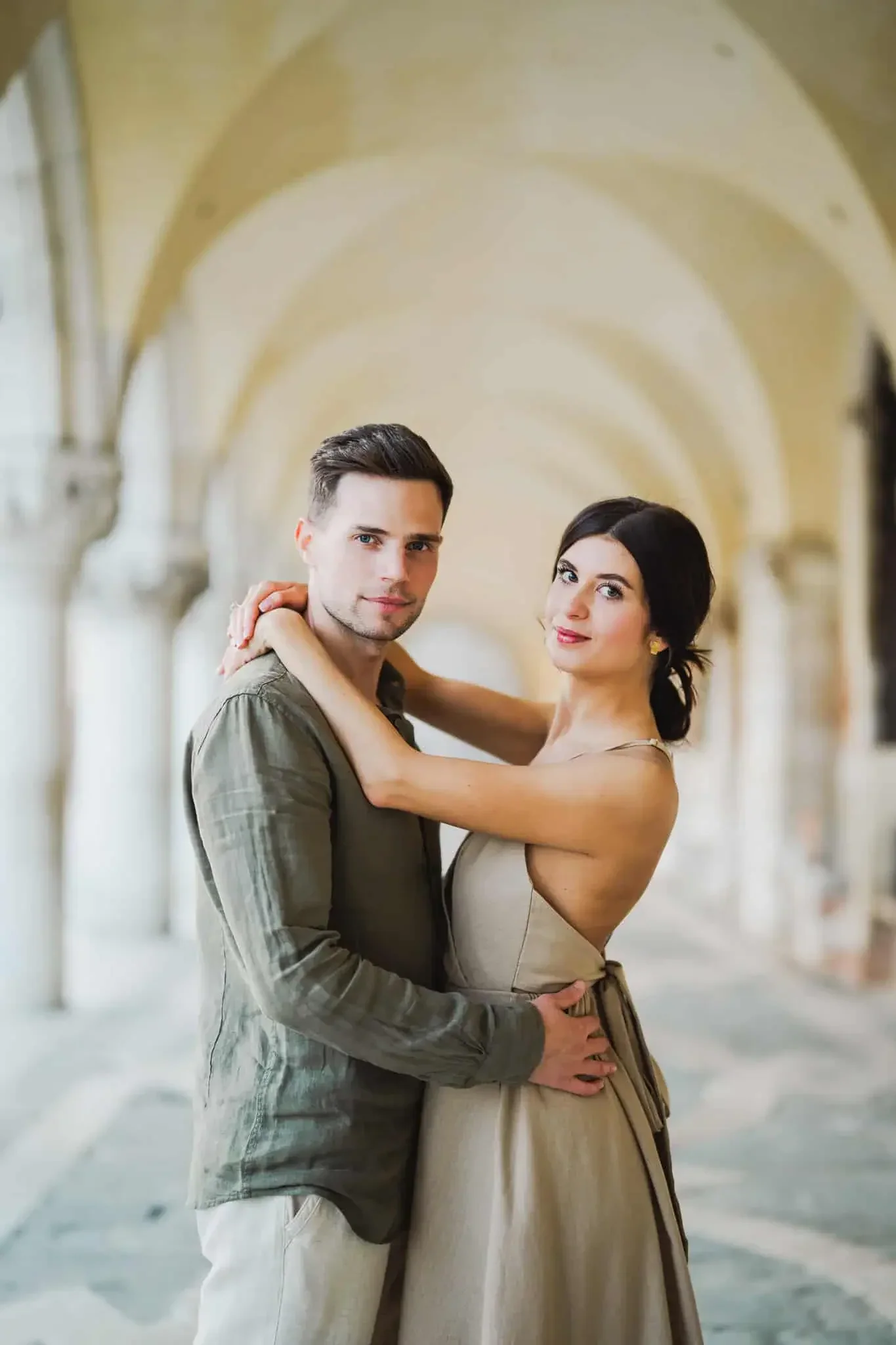 Elegant couple embracing in Venice arcade, romantic engagement photo shoot.