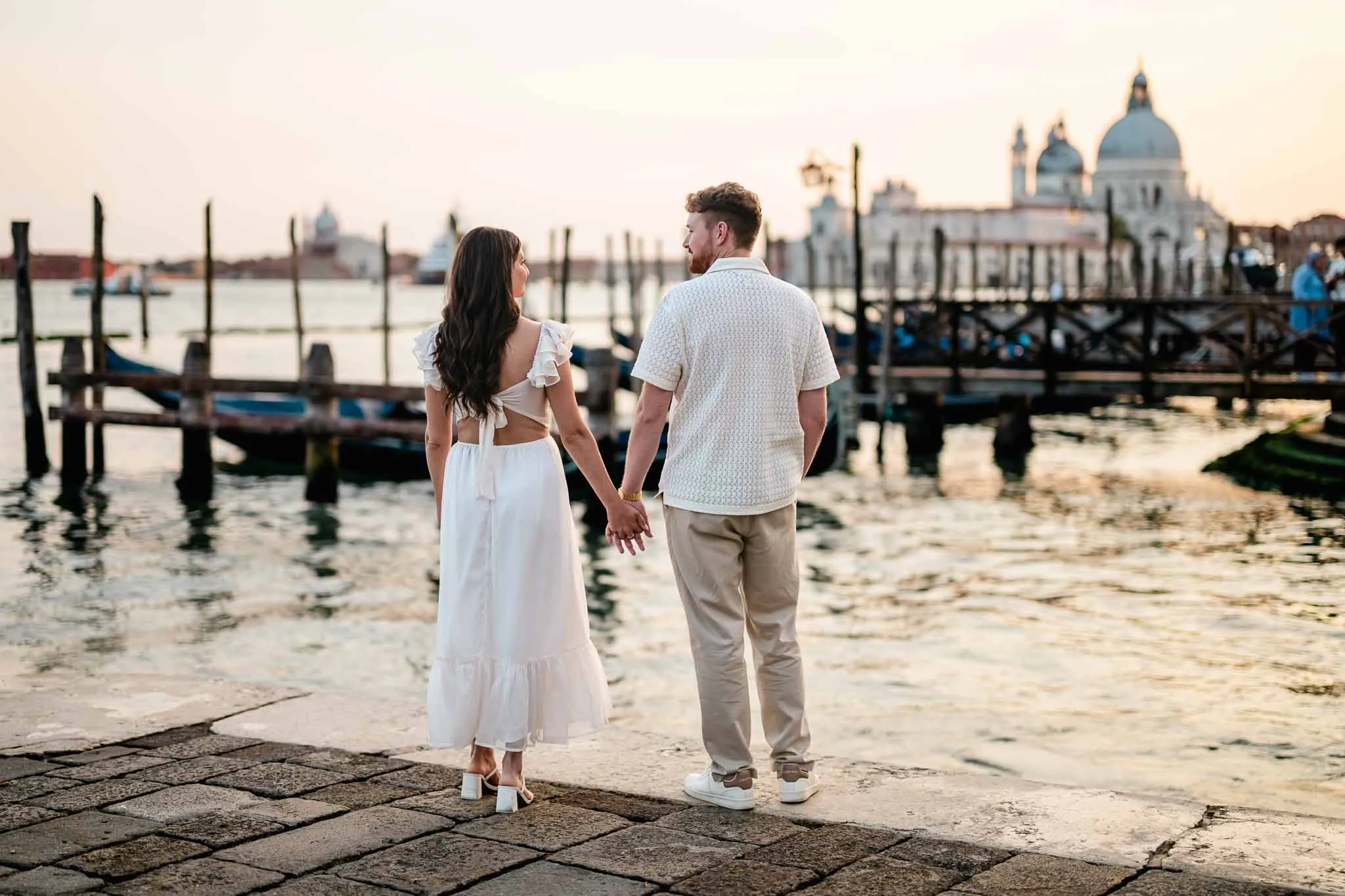 Romantic couple holding hands by Venice canal, sunset sky, historic architecture, wedding proposal, engagement photos.