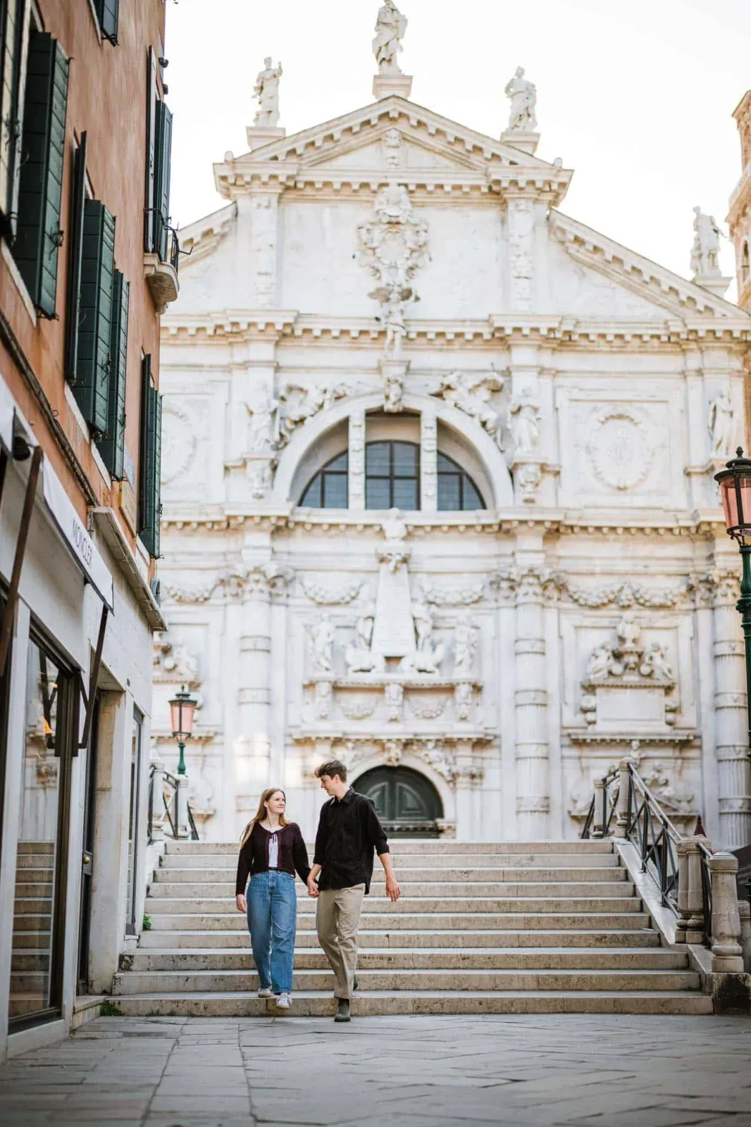Romantic couple walking down stairs in Venice, Italy, near historic architecture and charming streets.