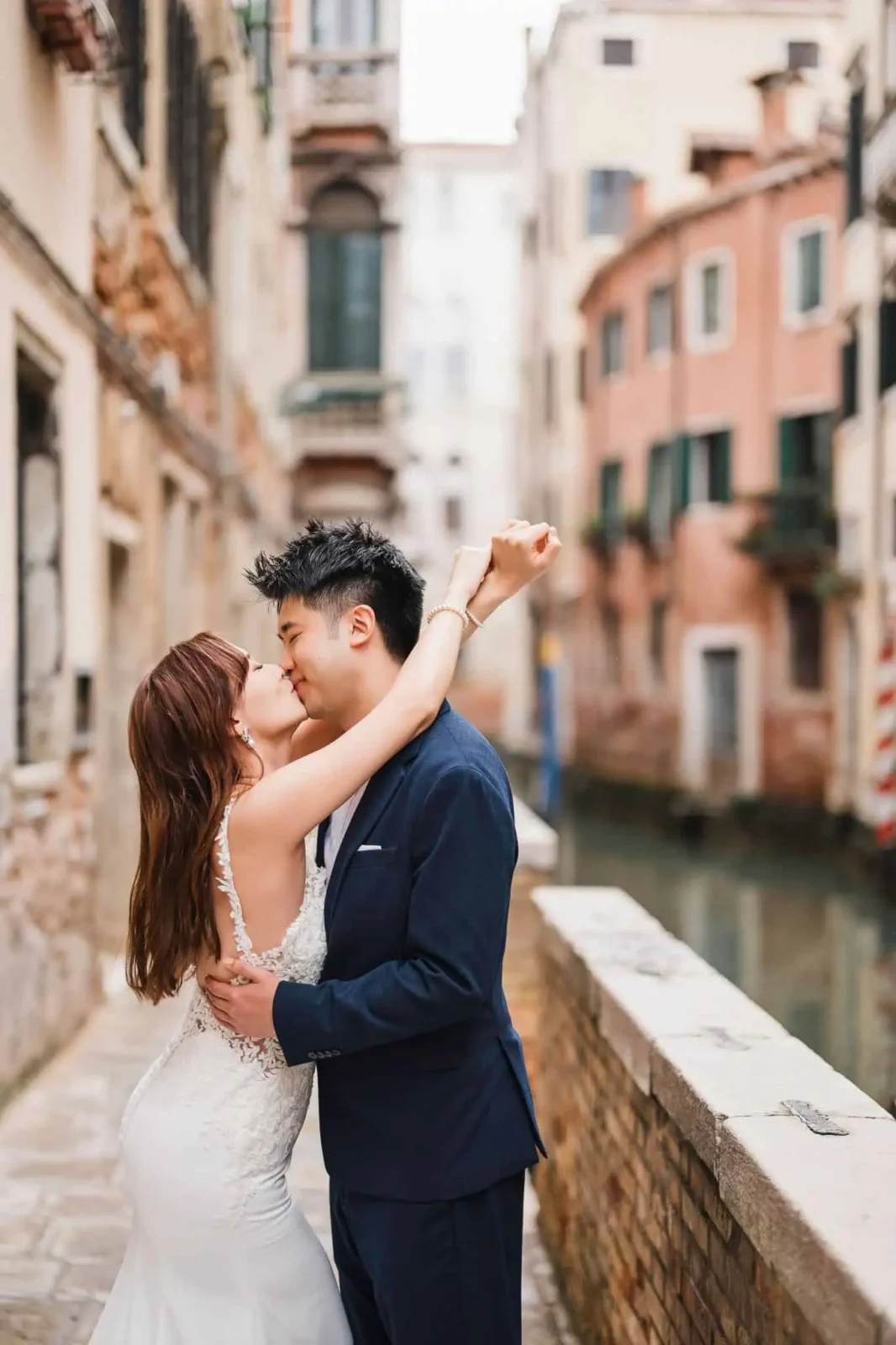 Elegant couple kissing in Venice, romantic wedding proposal on historic canal bridge.