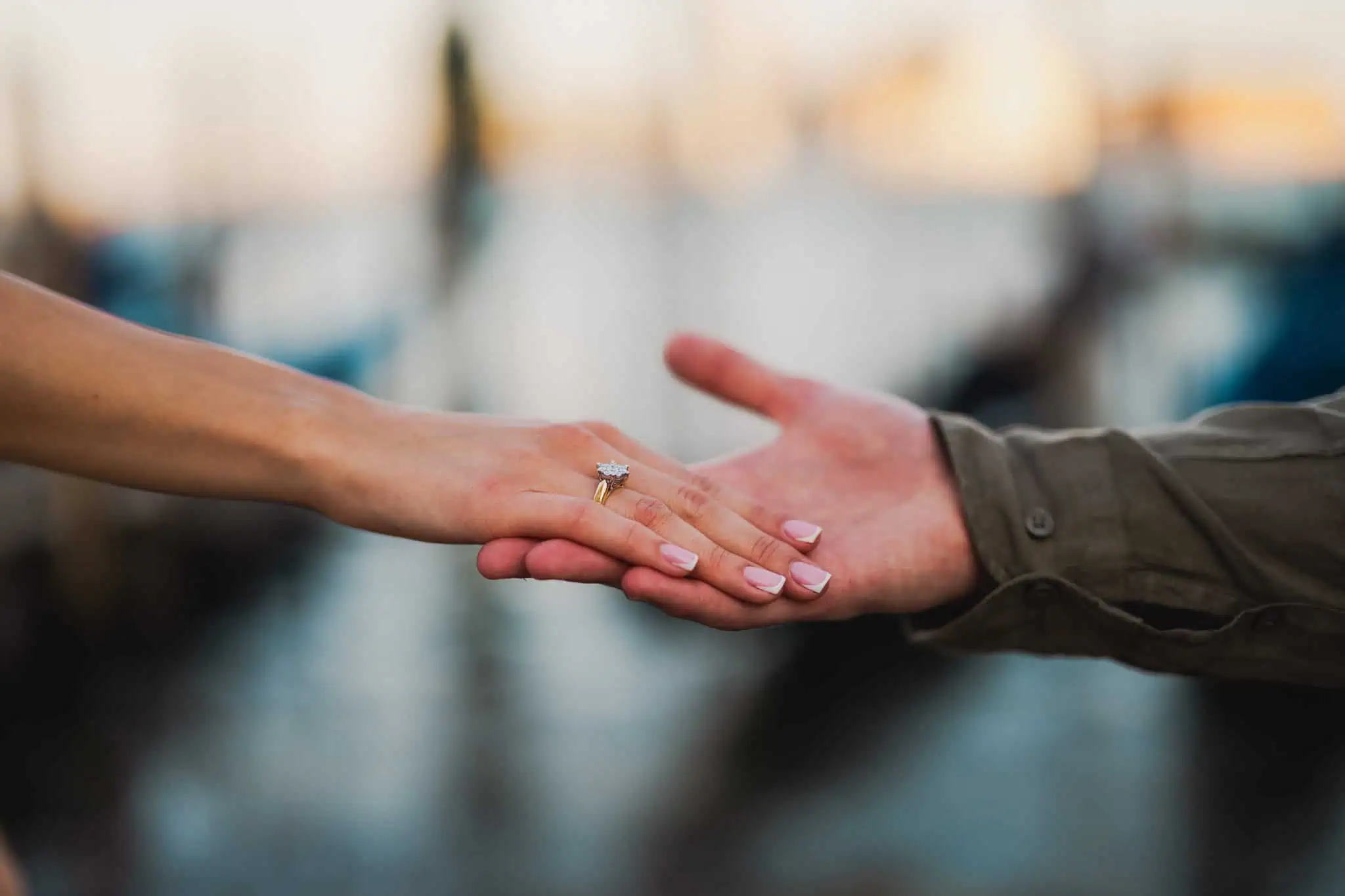 Delicate engagement ring on bride's finger with groom's hand reaching out, romantic Venice wedding moment.