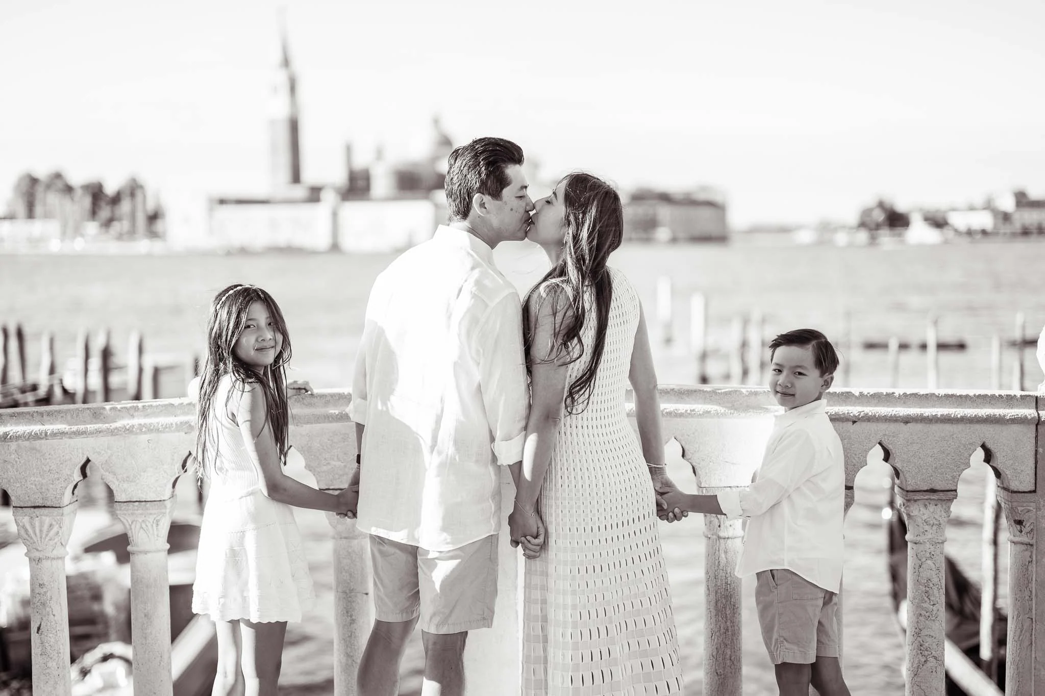 A couple kissing by the canal in Venice, with children holding hands nearby.