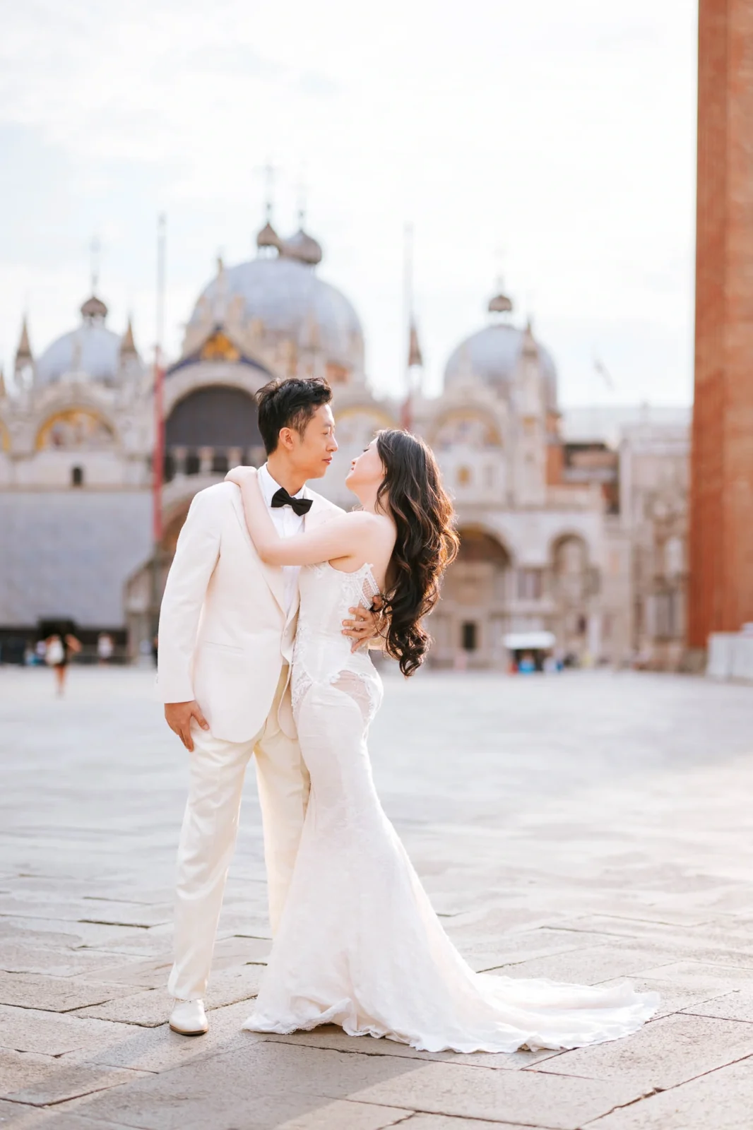 Elegant wedding couple embracing in Venice with historic architecture in the background.