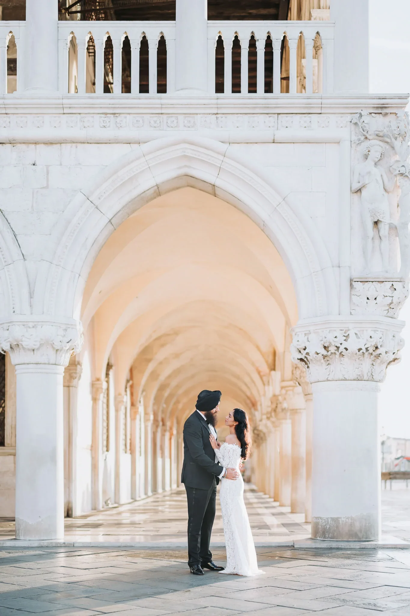 Elegant couple sharing a tender moment under Venice’s historic arches, captured by professional wedding and engagement photographer.