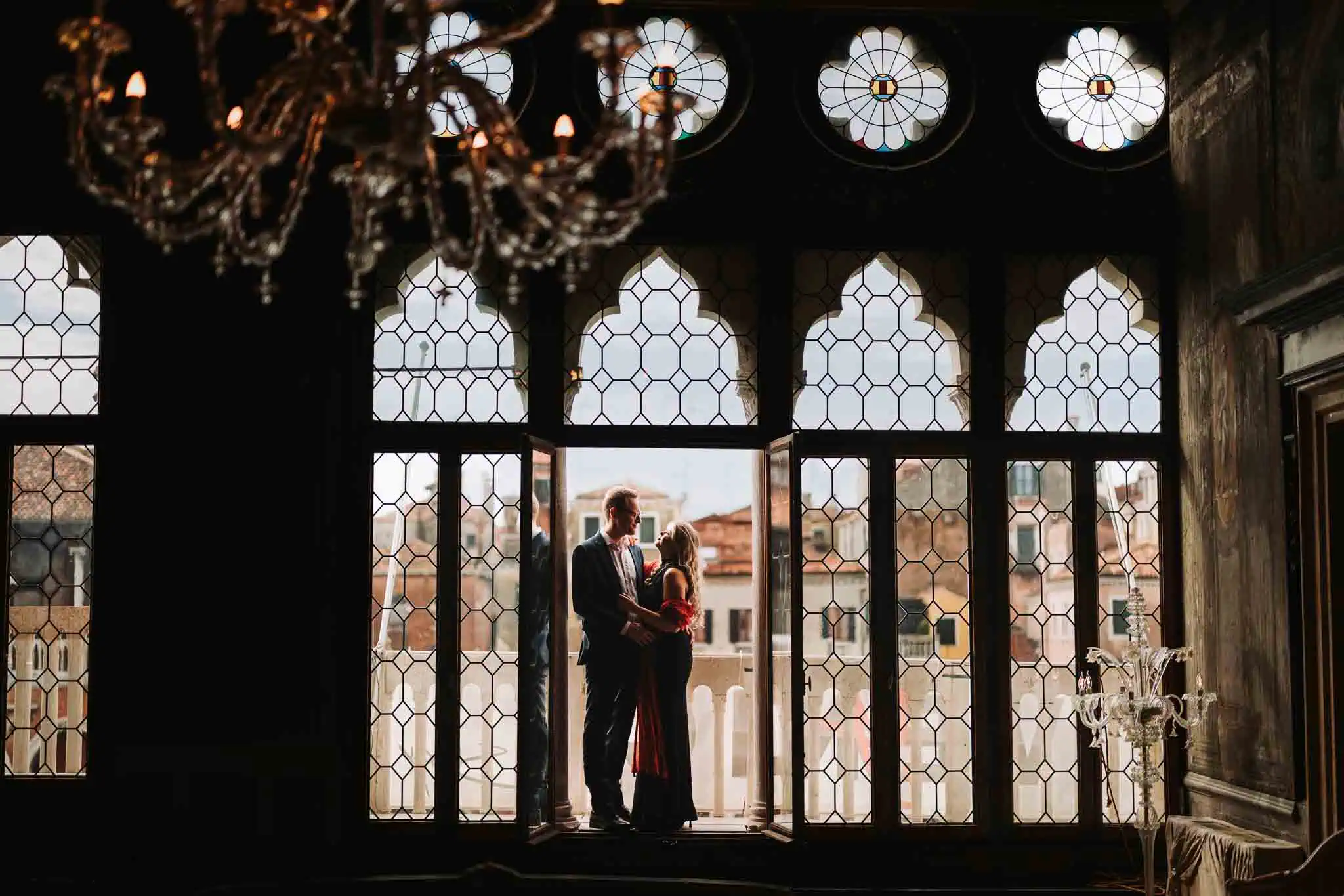 Elegant couple silhouette in Venetian window with historic city view at sunset.