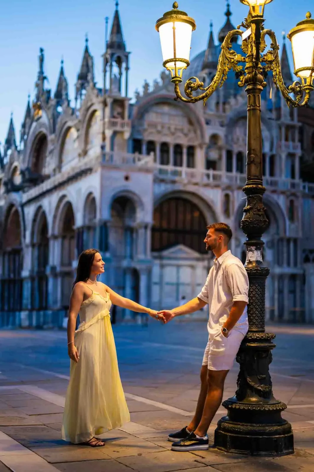 Romantic couple holding hands near Venice's historic architecture at dusk.