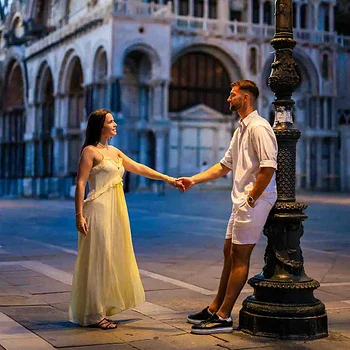 Romantic couple holding hands near Venice's historic architecture at dusk.