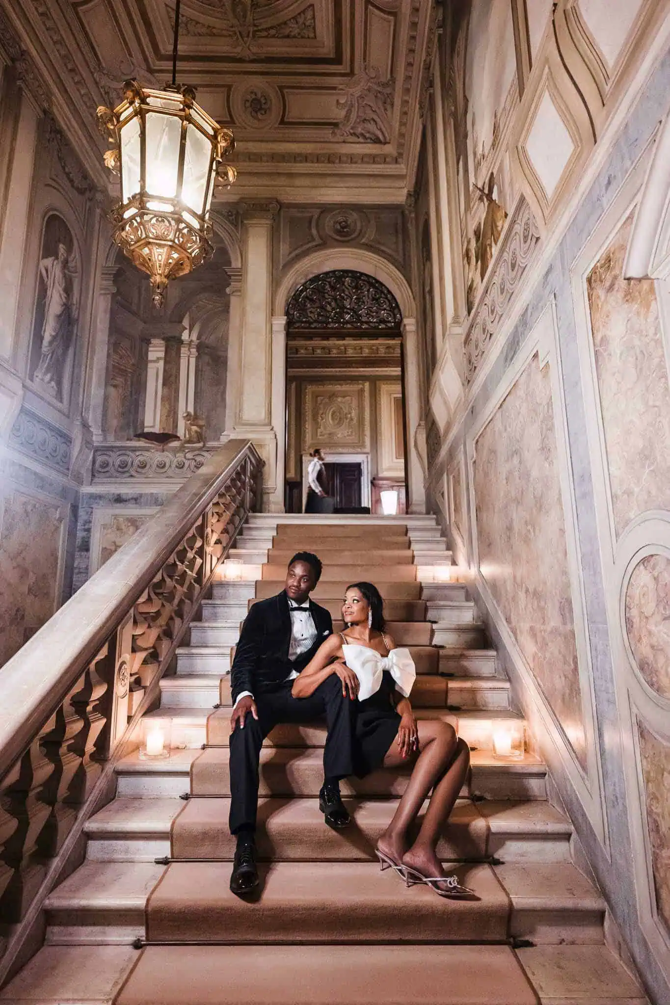 Elegant couple portraits on historic Venetian staircase with ornate architecture.