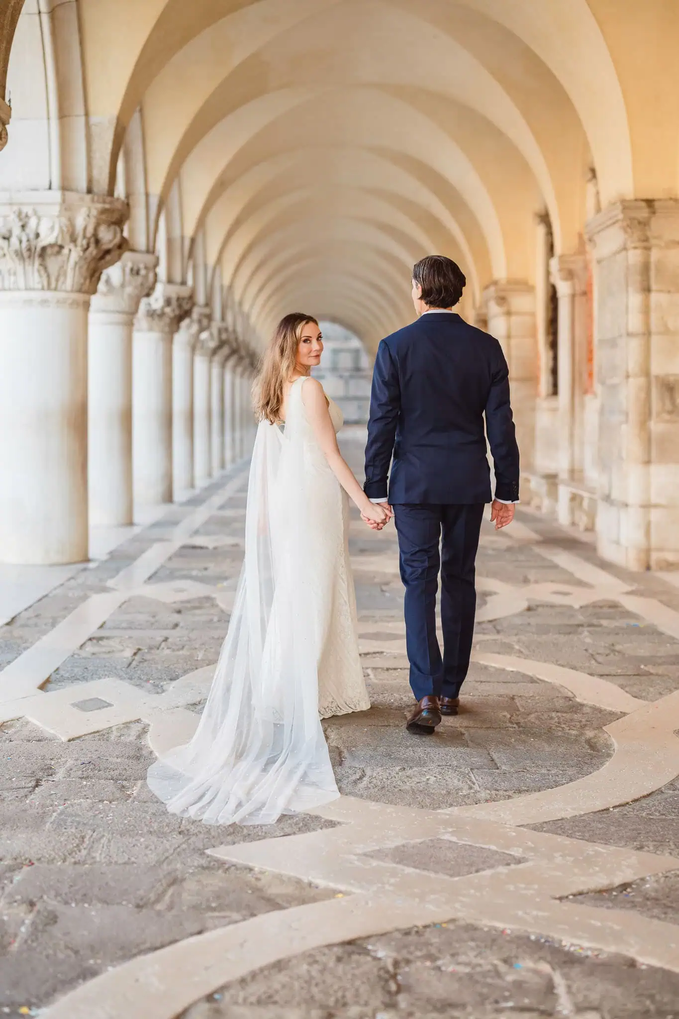 Elegant newlywed couple holding hands in Venice archway, romantic wedding photography.