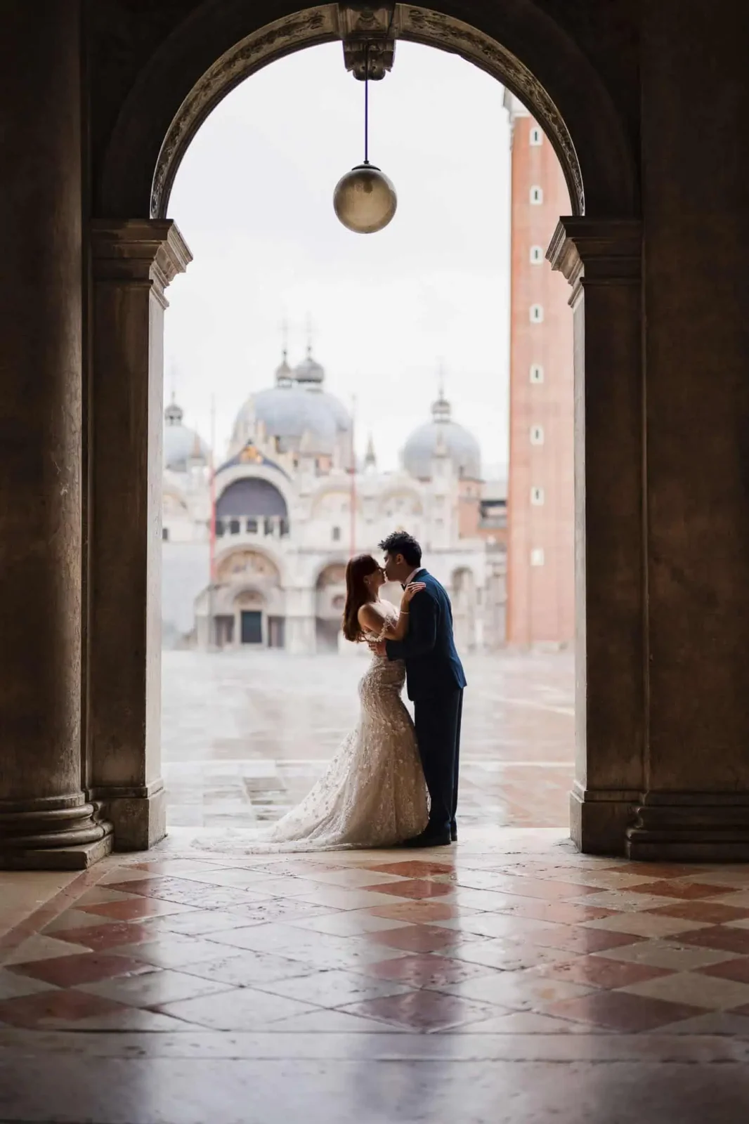 Elegant Venice wedding couple sharing a kiss under a historic archway with cityscape backdrop.