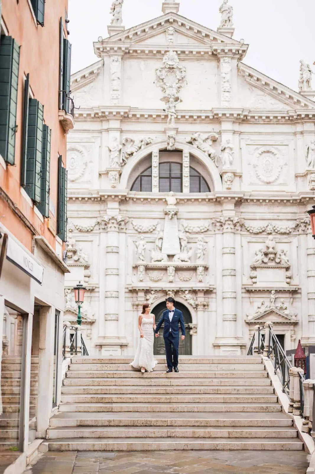 Elegant couple in wedding attire walking down Venice's historic church stairs, capturing romantic wedding moments.